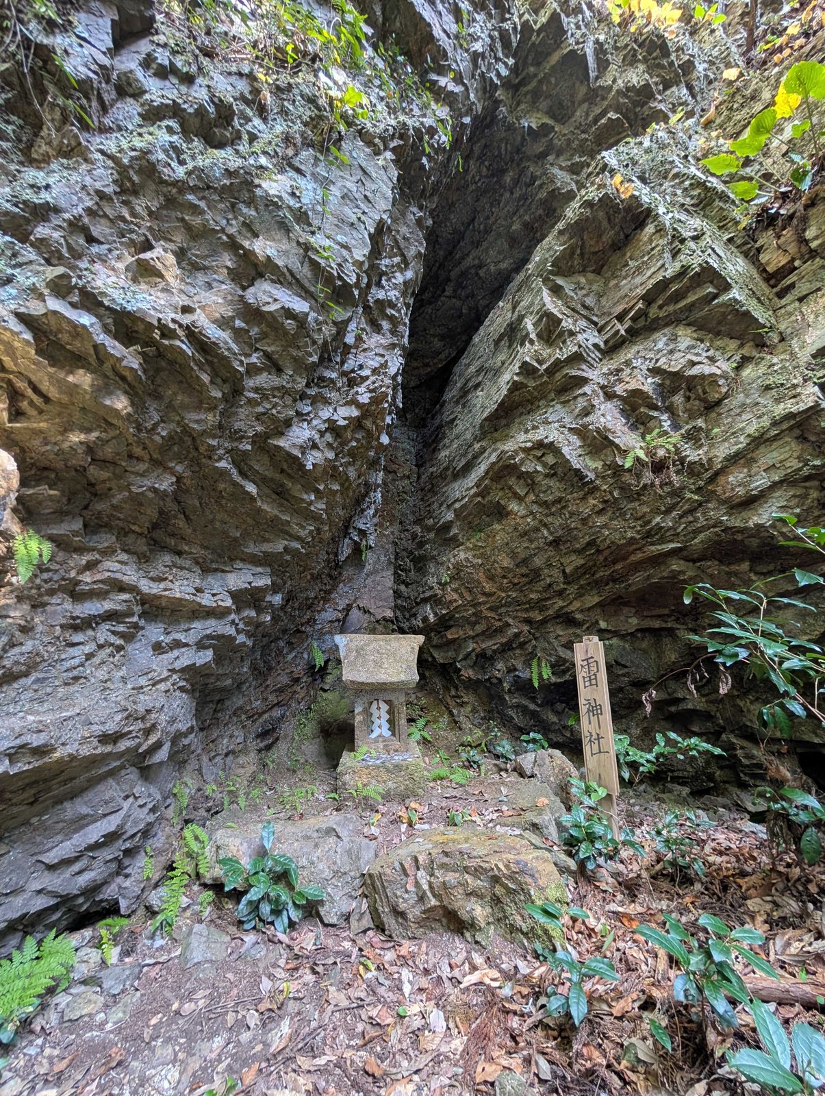 岩の裂け目の底に、小さな石の祠。脇の木札に「雷神社」とある
